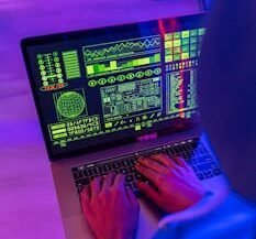 An unrecognizable person using a laptop indoors with digital screens displaying data and analytics.