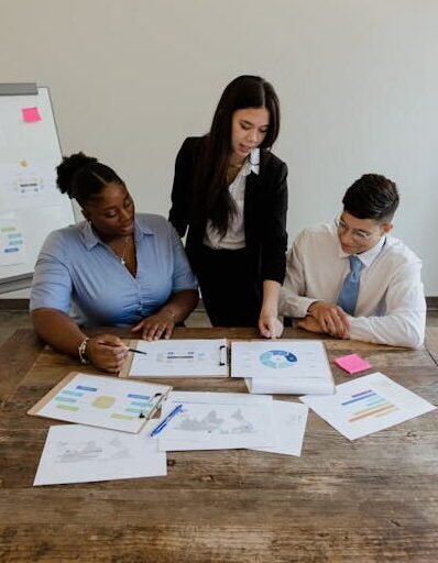 A focused business team engages in a meeting, discussing charts and graphs around a wooden table.